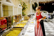Servicekraft in Tracht betreut ein warmes Buffet im Veranstaltungssaal der Hoftaverne