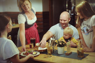 Servicekraft in Tracht serviert einer Familie am Tisch ein Gericht in der Hoftaverne