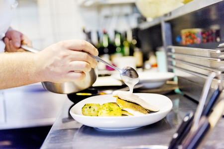 Arbeiten in der Küche der Hoftaverne Ziegelböck – Anrichten mit Sorgfalt Koch richtet in der Küche der Hoftaverne Ziegelböck ein Gericht an und gibt Sauce über den Teller