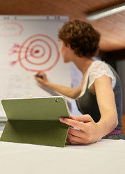 Person schreibt auf ein Flipchart waehrend eines Workshops, im Vordergrund ein Tablet auf dem Tisch